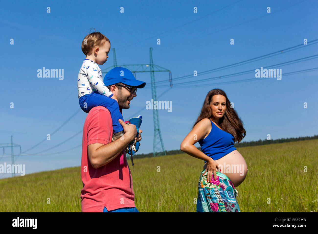 Schwangere Frau, Familie, Mutter, Vater und Sohn im Sommer Wiese mit Stromleitungen Stockfoto