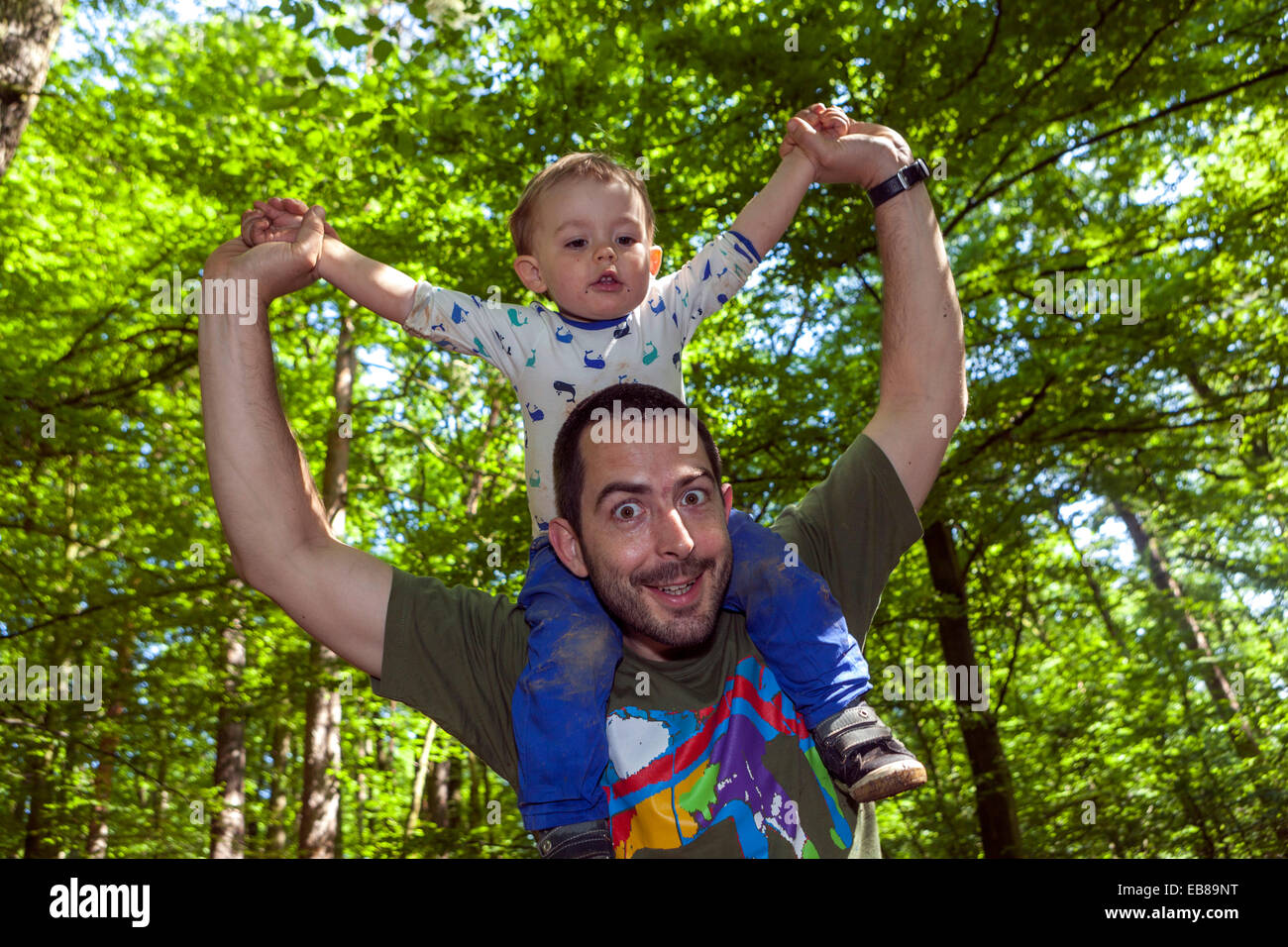 Glücklicher Vater trägt Sohn auf Schultern unter Bäumen grüne Szene Stockfoto