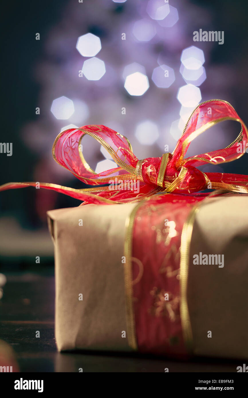 Rustikale Christmas Present, rote Schleife und unscharfen Lichter im Hintergrund Stockfoto