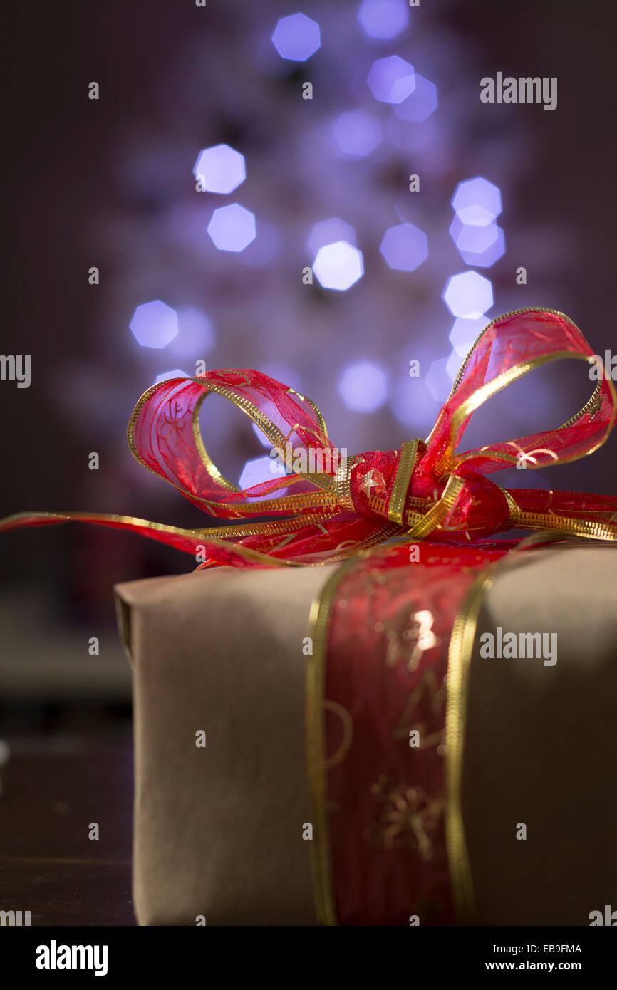 Rustikale Christmas Present, rote Schleife und unscharfen Lichter im Hintergrund Stockfoto