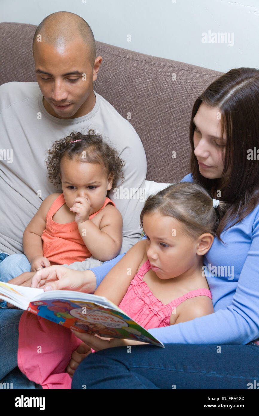 Junge Familie sitzt auf dem Sofa zusammen lesen, Stockfoto