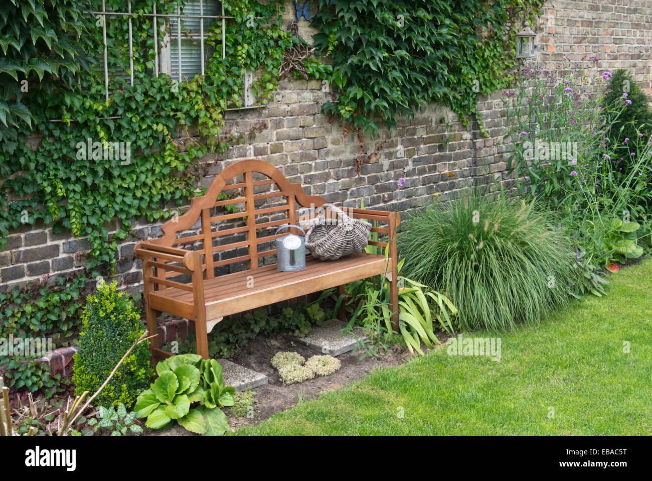 Holzbank mit Gießkanne und Korb in einem beständigen Garten Stockfoto