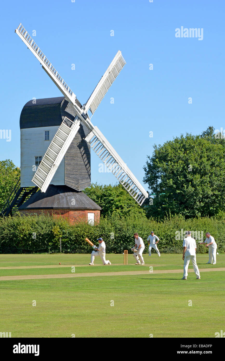 Land ikonischen Quintessenz England idyllische Dorf grünen Cricket Match Bowler Batsman & Fielder Mountnessing Post Mill Brentwood Essex Landschaft Stockfoto