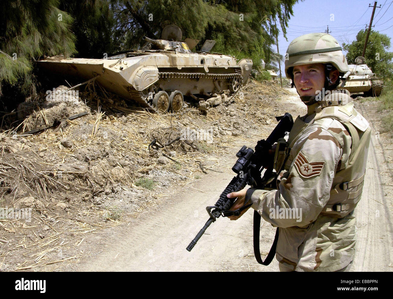OPERATION IRAQI FREEDOM - Staff Sgt Brandon Storey sichert eine Straße neben einem zerstörten irakischen gepanzerten-Mannschaftswagen während einer Stockfoto