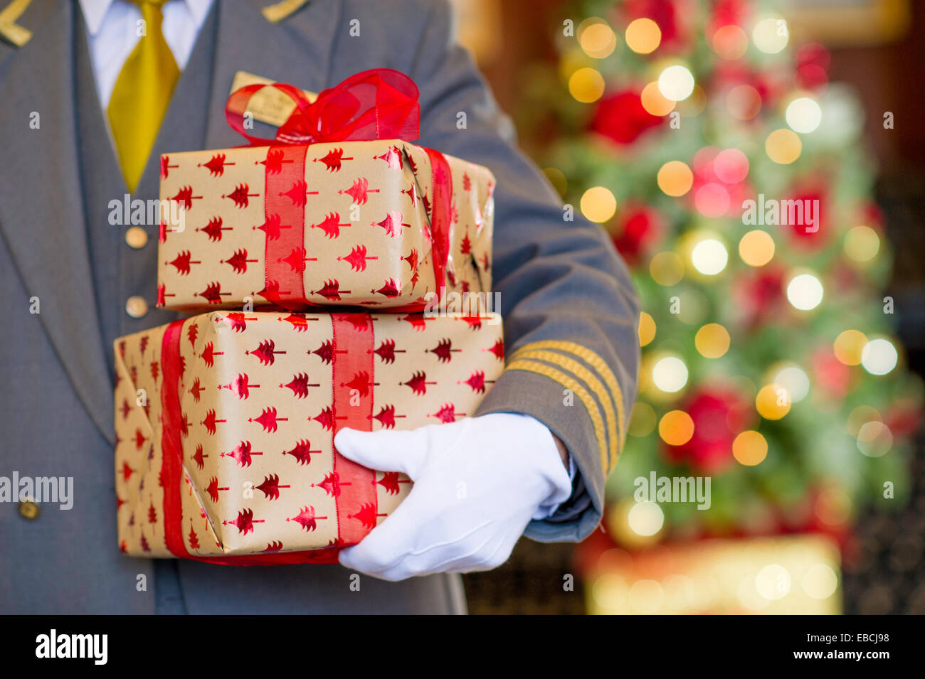 Türsteher halten Weihnachtsgeschenke mit Weihnachtsbaum im Hintergrund Stockfoto