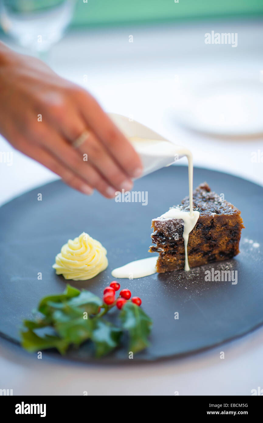 Gießen die Creme über Christmas Pudding mit Holly im Vordergrund. Stockfoto