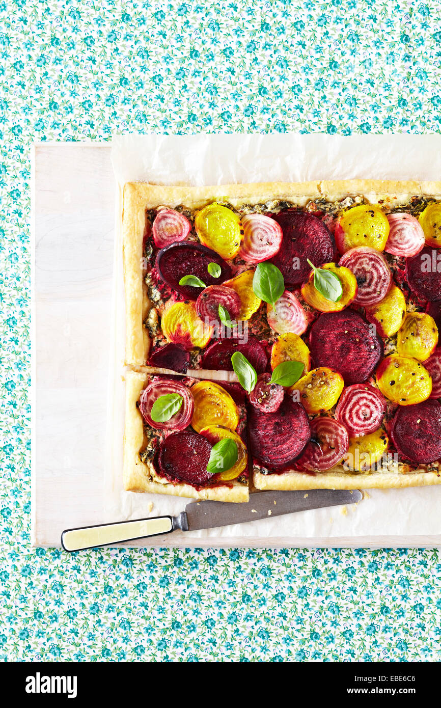 Rot, gelb und gestreiften Rüben-Tarte mit frischen Basilikum auf weißen Holzbrett mit Messer auf Floral Background, Studio gedreht Stockfoto