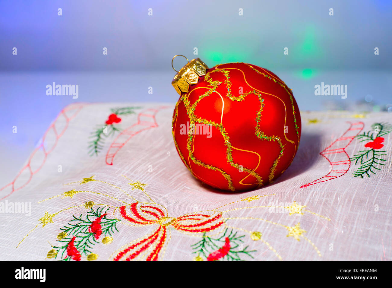 Rote Weihnachtskugel auf festliche Servietten mit Stickerei auf blauem Hintergrund Stockfoto