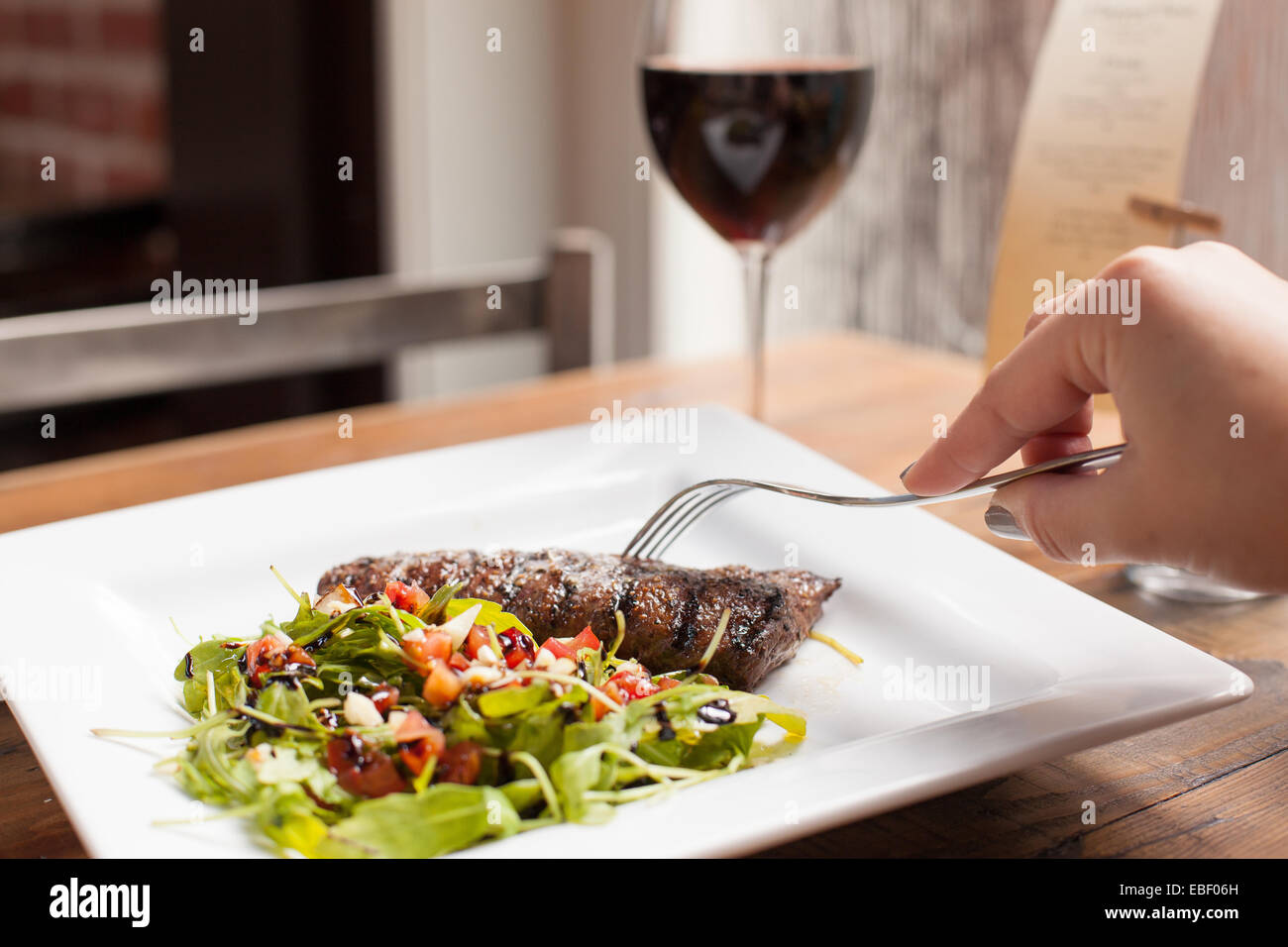 Weibliche Hand mit Gabel und gegrilltes Steak mit Rotwein Stockfoto