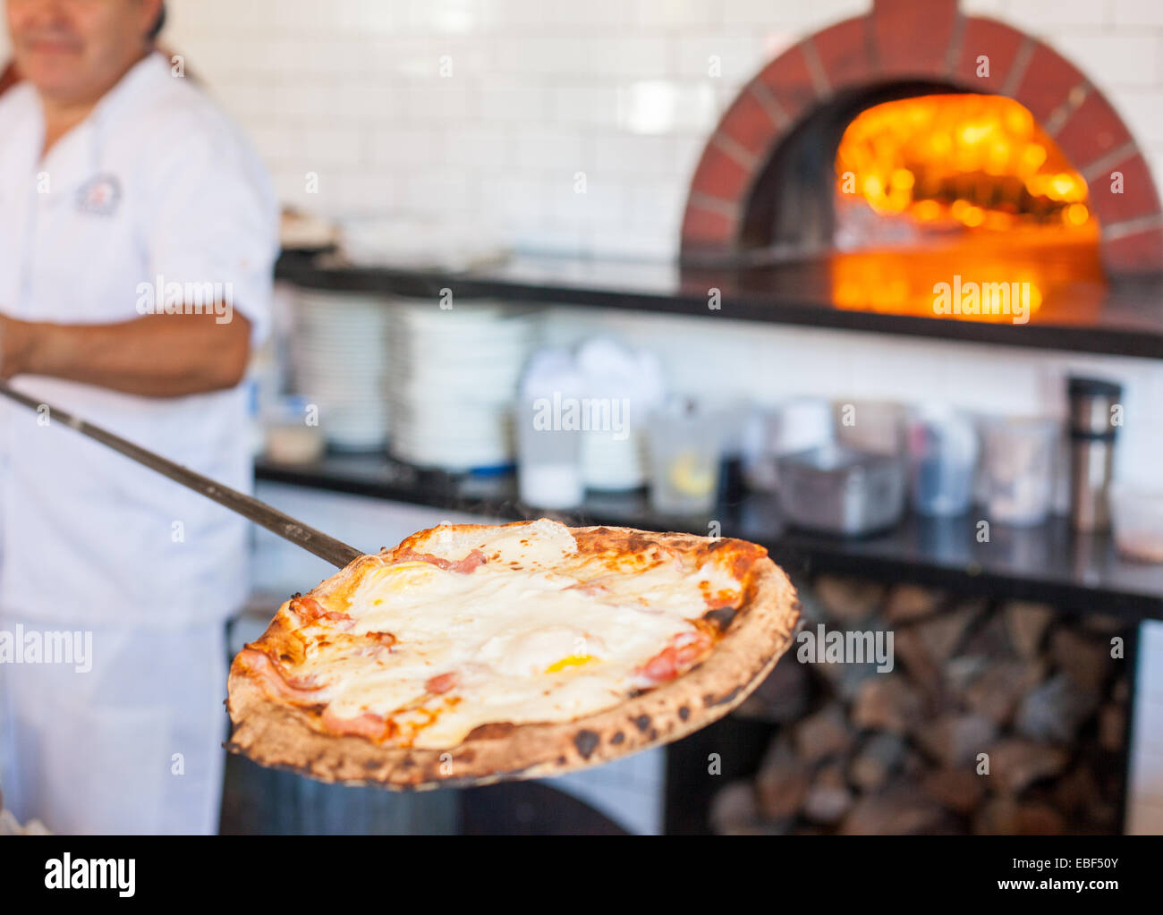 Man zieht Pizza Paddel aus einem Holzofen Stockfoto