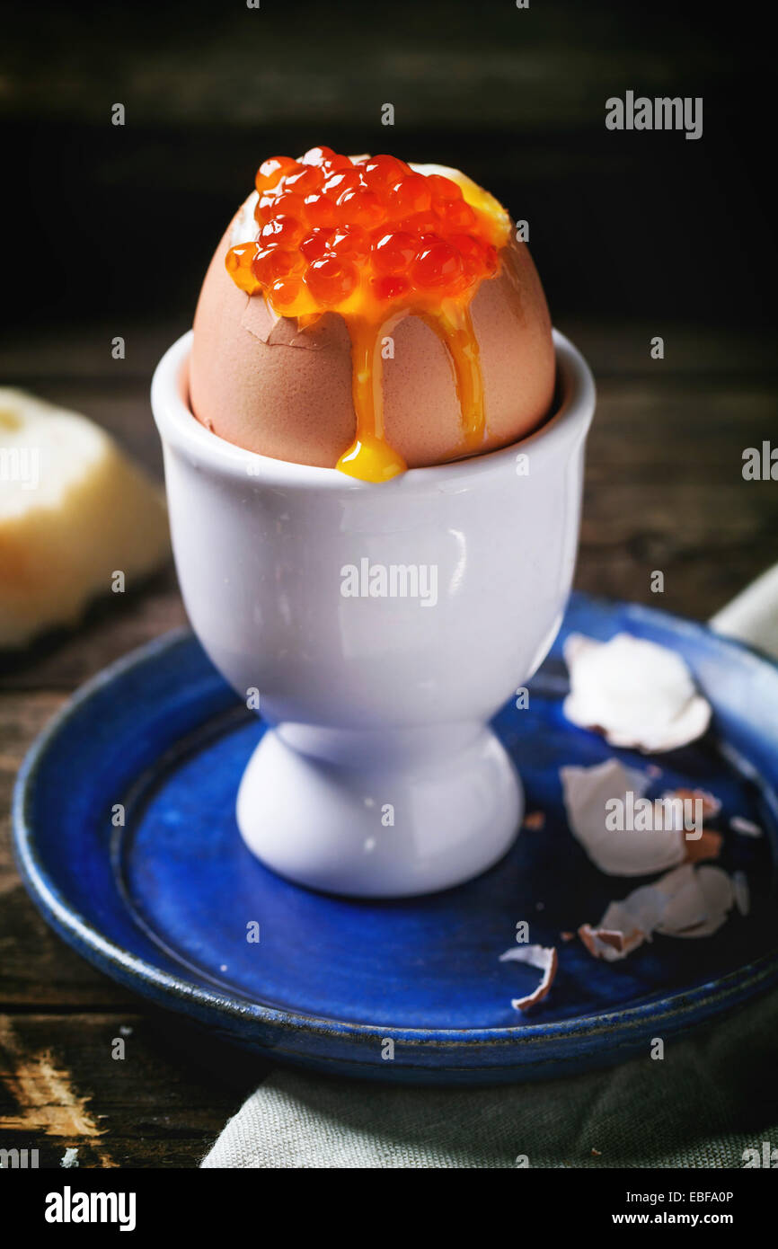Frühstück mit wachsweiches Ei mit rotem Kaviar in weiß Eierbecher über alten Holztisch mit Brot serviert. Serien ansehen Stockfoto
