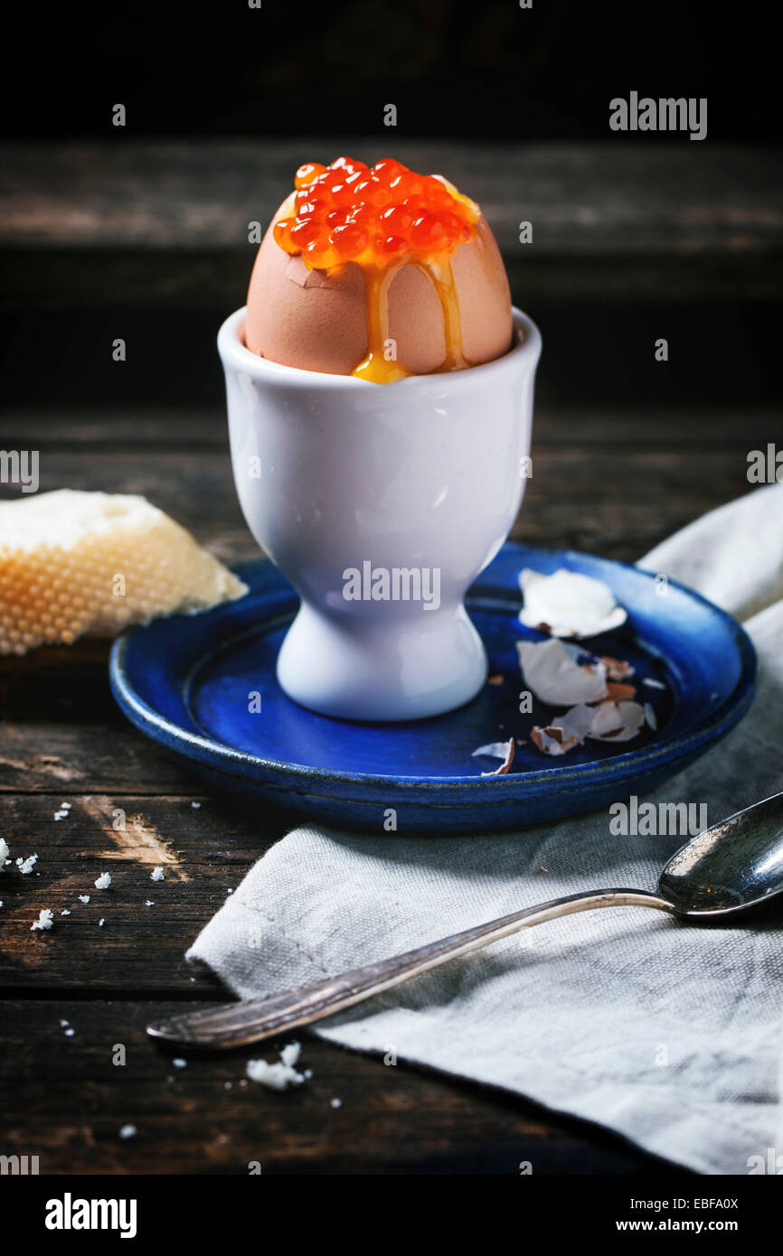 Frühstück mit wachsweiches Ei mit rotem Kaviar in weiß Eierbecher über alten Holztisch mit Brot serviert. Serien ansehen Stockfoto