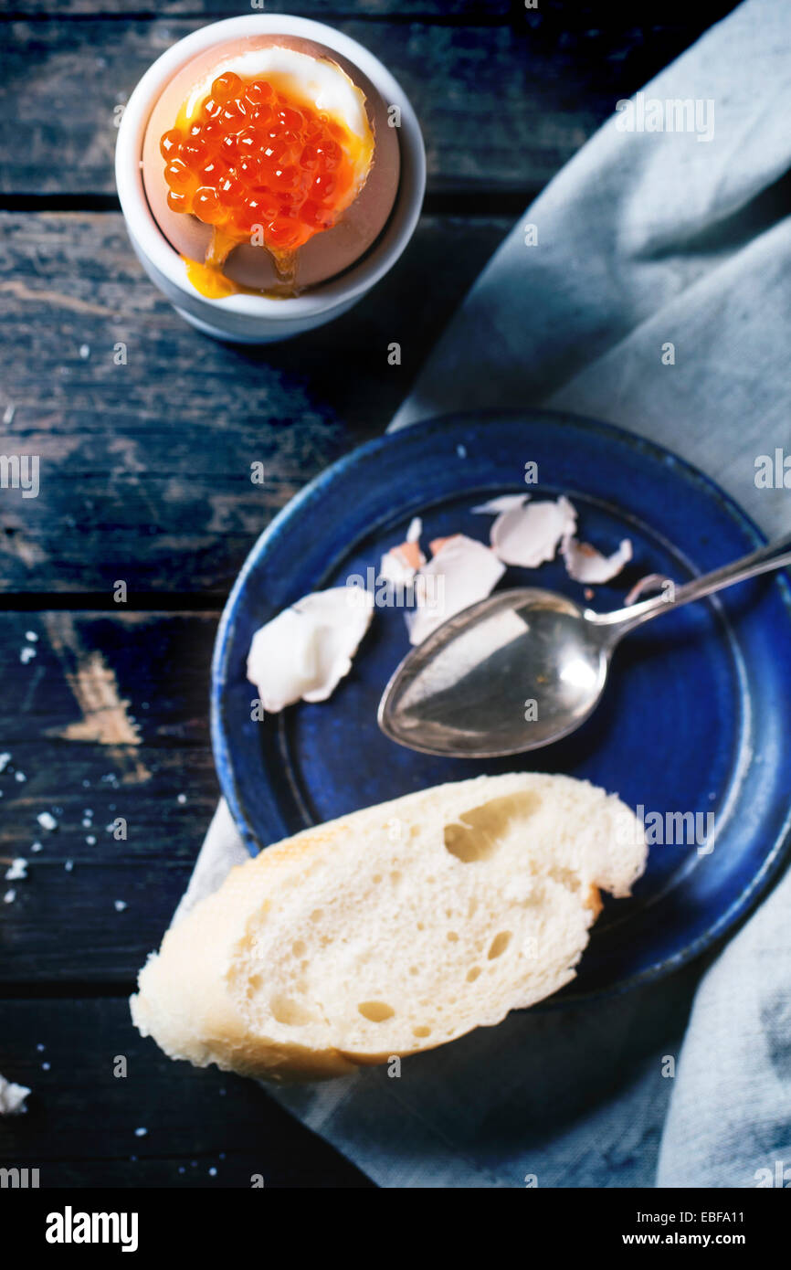 Frühstück mit wachsweiches Ei mit rotem Kaviar in weiß Eierbecher über alten Holztisch mit Brot serviert. Fokus auf Kaviar. Stockfoto