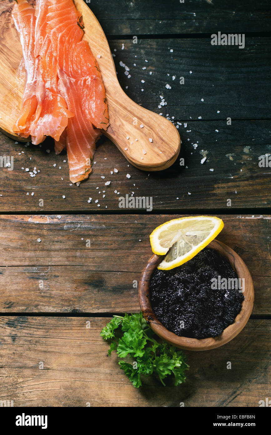 Schale mit schwarzem Kaviar und Stücke von gesalzenen Lachs auf Oliven Holzplatte mit Vintage Messer über alten Holztisch. Ansicht von oben. Stockfoto