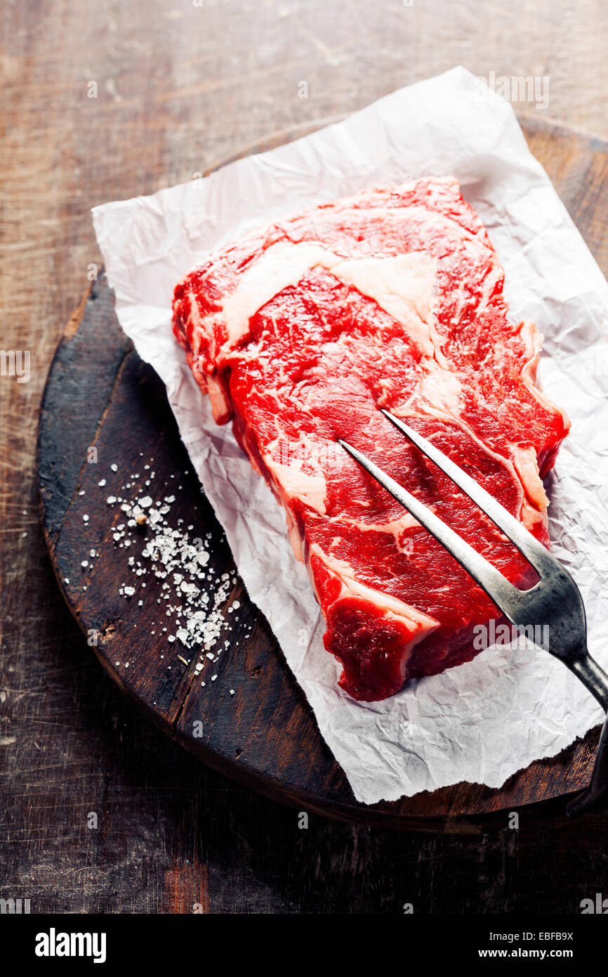Rohes Rindfleischsteak mit Fleischgabel auf einem alten Holztisch Stockfoto