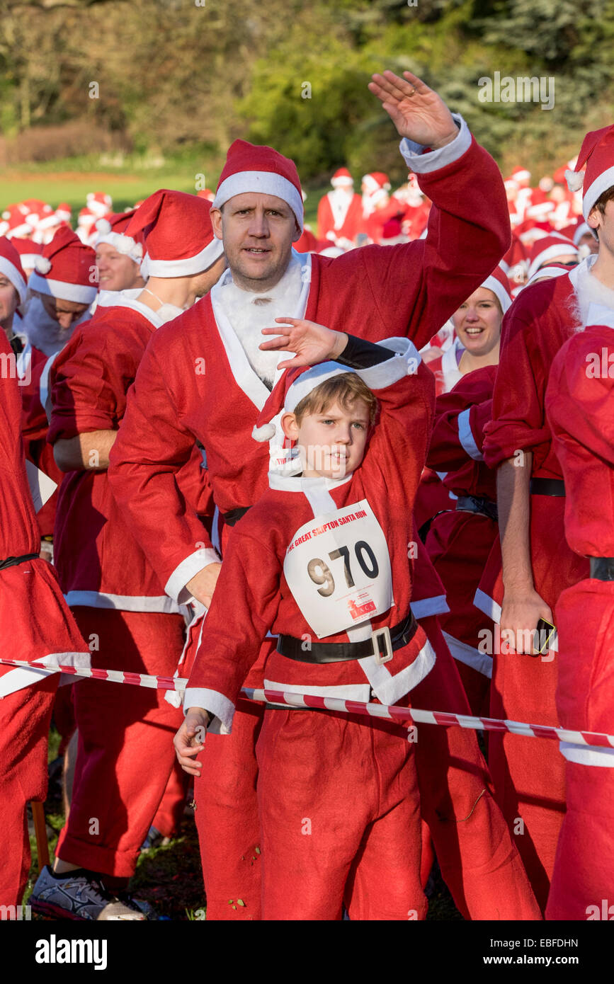 Menschen (Männer, Frauen und Kinder) Gekleidet in rot & weiß Vater Weihnachten Outfits mit Hüte & falsche Bärte, Stehen, warten Teil in der Großen Skipton Santa Fun Run, eine jährliche fundraising Charity Rennen vom Rotary Club - Aireville Park, Skipton Stadtzentrum, dem North Yorkshire, England, UK organisiert wird. Stockfoto