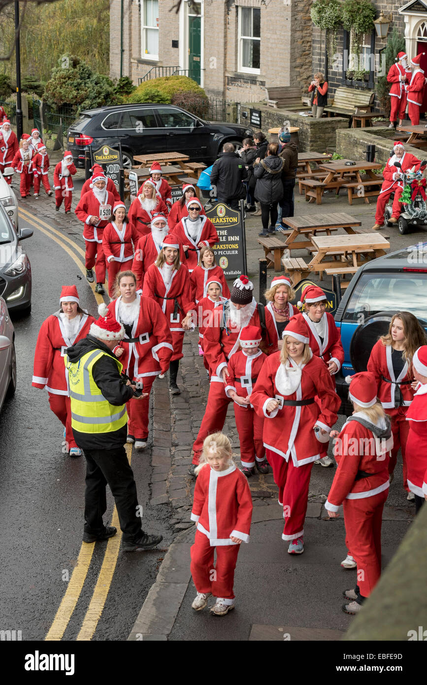 Menschen (Männer, Frauen und Kinder) in rot & weiß Vater Weihnachten Outfits gekleidet sind Wandern, Joggen, Laufen und die Teilnahme an der großen Skipton Santa Fun Run, eine jährliche fundraising Charity Rennen vom Rotary Club - Skipton Stadtzentrum, dem North Yorkshire, England, Großbritannien organisiert. Stockfoto