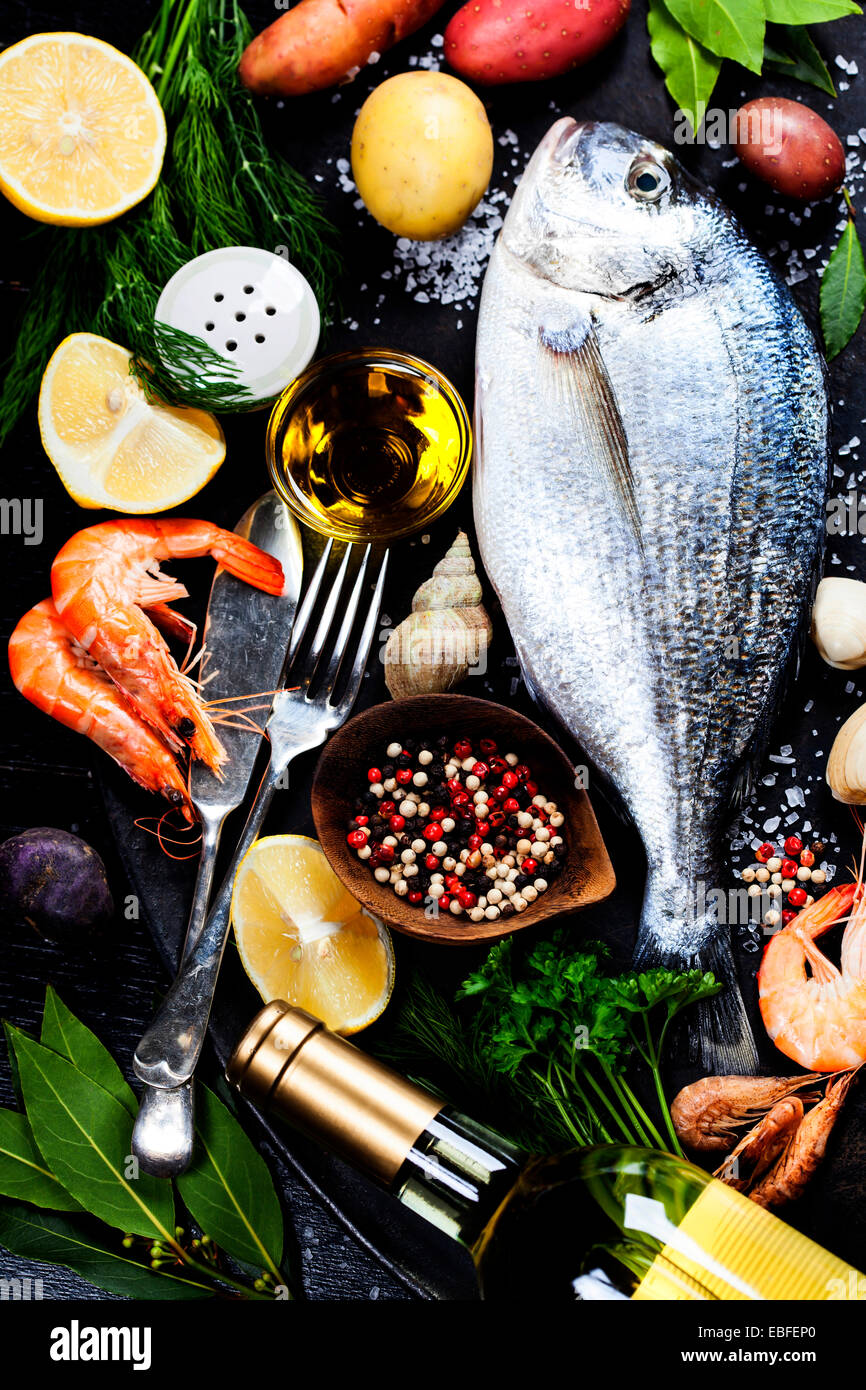 Köstlichen frischen Fisch und Meeresfrüchte auf dunkle Vintage-Hintergrund. Fisch, Herzmuscheln und Garnelen mit aromatischen Kräutern, Gewürzen & Gemüse Stockfoto