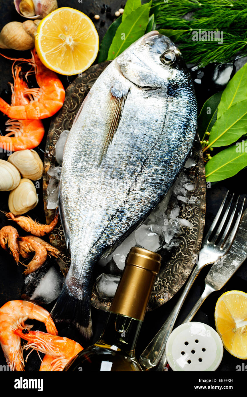 Köstlichen frischen Fisch und Meeresfrüchte auf dunkle Vintage-Hintergrund. Fisch, Herzmuscheln und Garnelen mit aromatischen Kräutern, Gewürzen & Gemüse Stockfoto