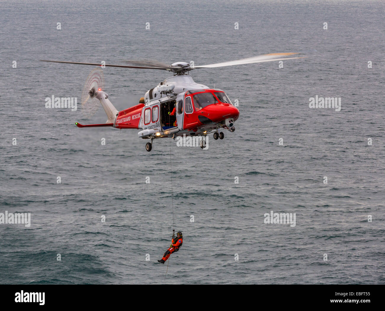 Ein Blick auf einen Such- und Rettungshubschrauber der Augusta HM Coastguard mit dem Winzer, der auf das Meer abgesenkt ist, den englischen Kanal, England Großbritannien Stockfoto