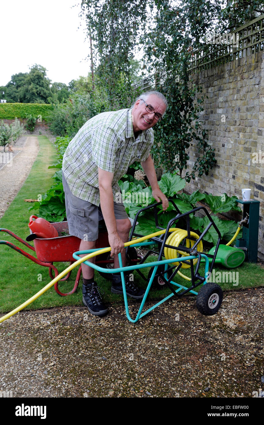 Mann, die verwinkelten Garten Gartenschlauch auf Trolley - Freiwillige in Chiswick House Küchengarten, London Borough of Hounslow Stockfoto