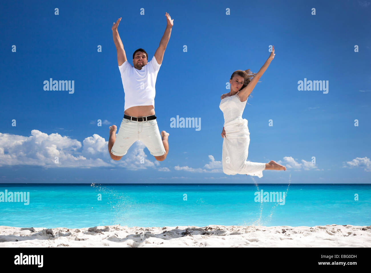Glückliche Brautpaar sprang am Strand mit blauer Himmelshintergrund Stockfoto