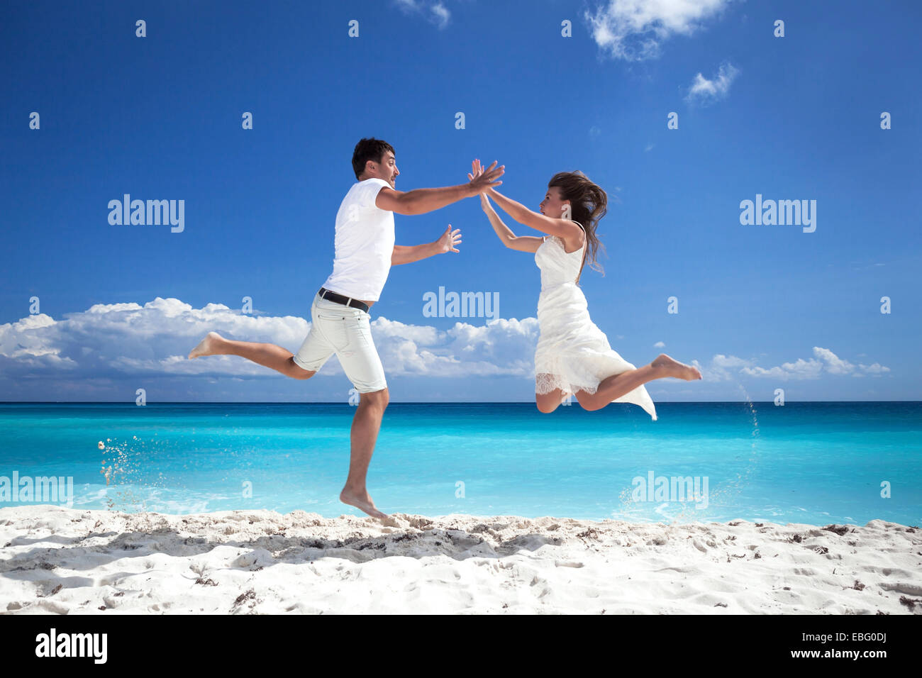 Glückliche Brautpaar sprang am Strand mit blauer Himmelshintergrund Stockfoto