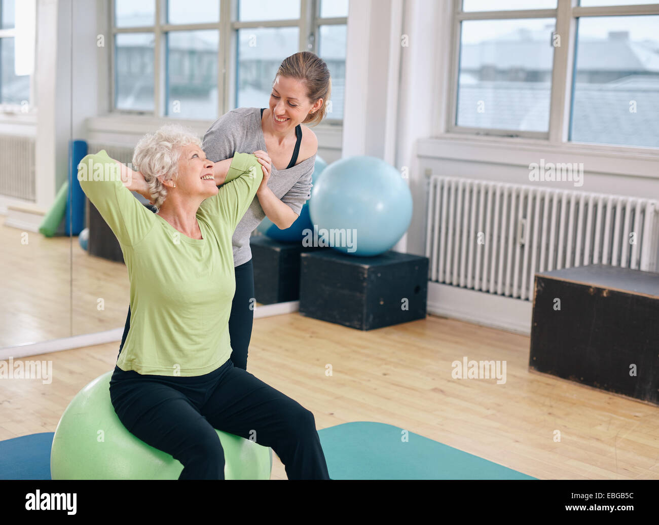 Reife Frau auf einer Fitness-Ball mit Hilfe von personal Trainer im Fitness-Studio trainieren. Beautiful senior Woman Training mit Instruktor Stockfoto