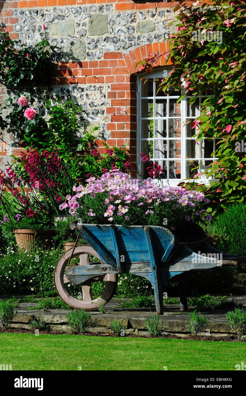 Eine Schubkarre voller Blumen in einen Bauerngarten. UK Stockfoto