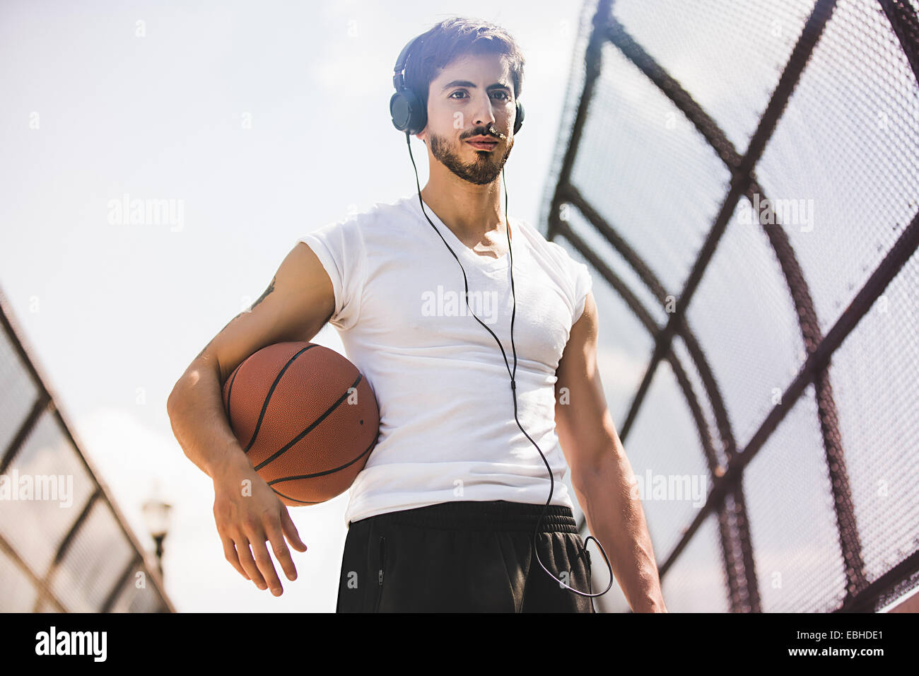 Junge männliche Basketballspieler zu Fuß entlang Fußgängerbrücke Kopfhörer anhören Stockfoto