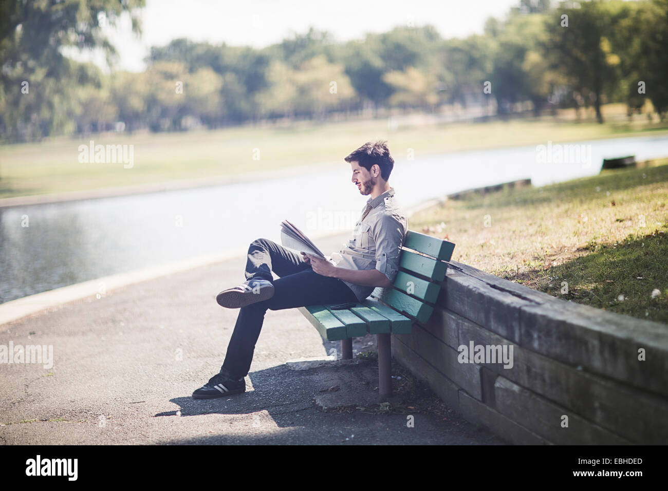 Junger Mann liest Zeitung auf Bank im park Stockfoto
