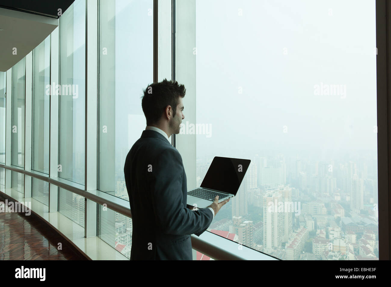 Junger Geschäftsmann mit Laptop aus Wolkenkratzer Bürofenster, Shanghai, China Stockfoto