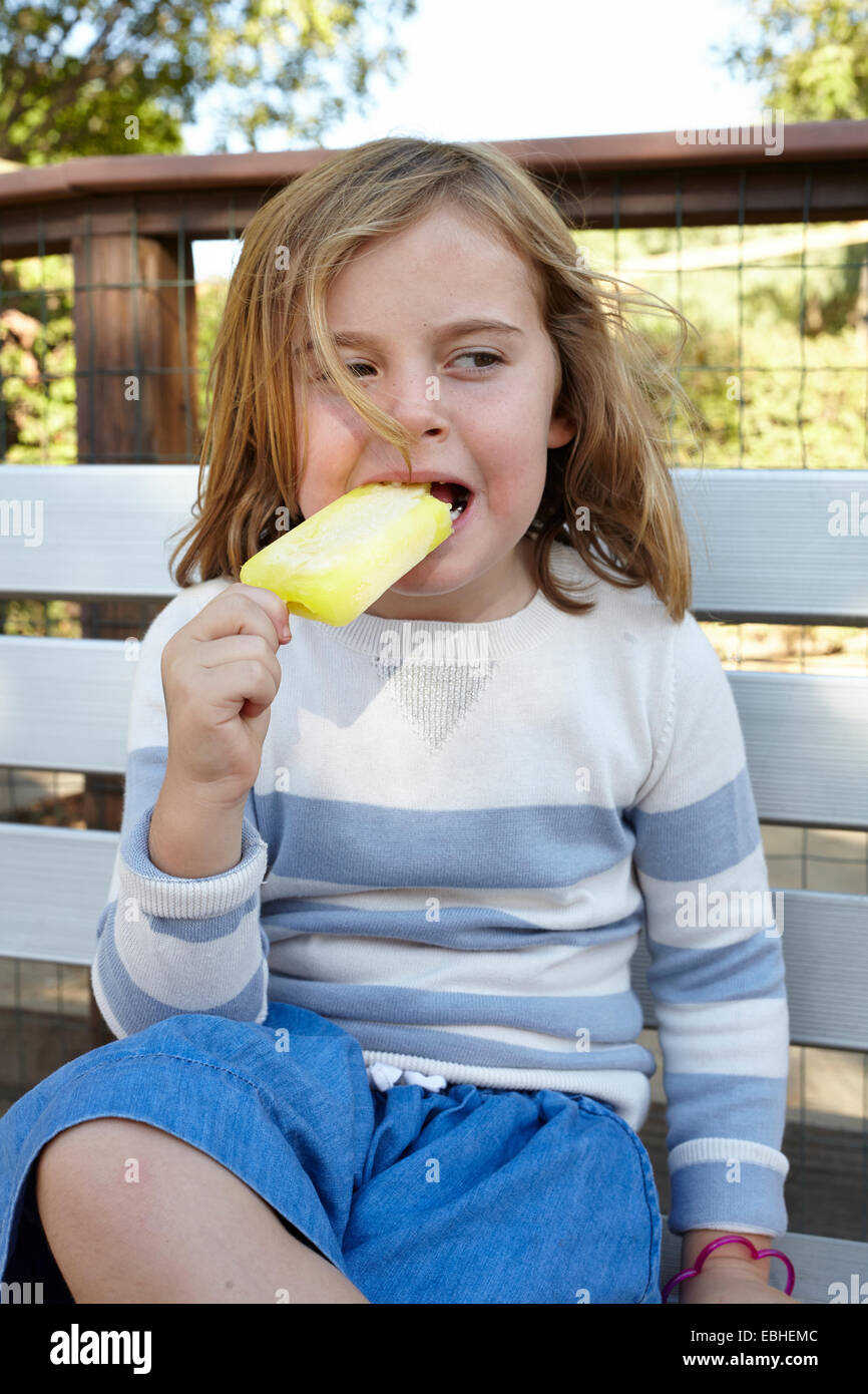 Porträt eines Mädchens essen Eis am Stiel auf Gartenbank Stockfoto
