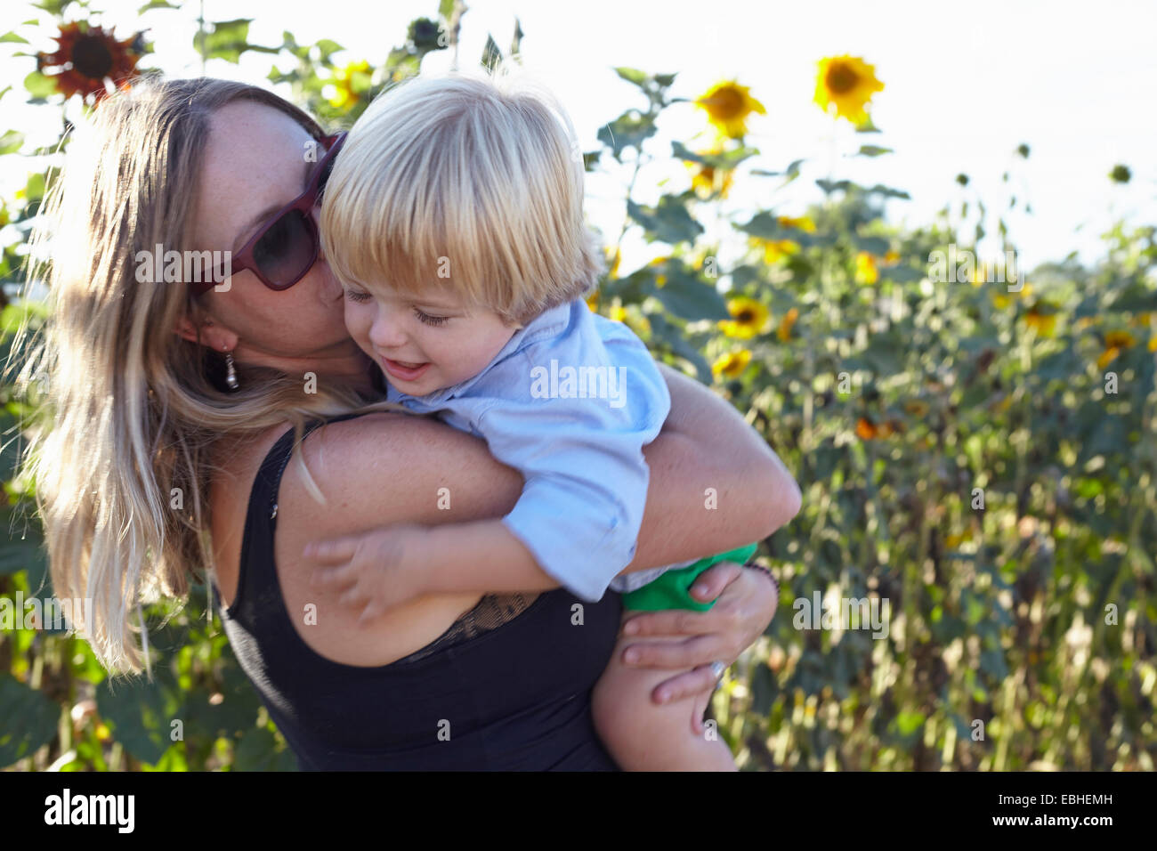 Mitte Erwachsene Frau und Kind umarmt im Sonnenblumenfeld Stockfoto