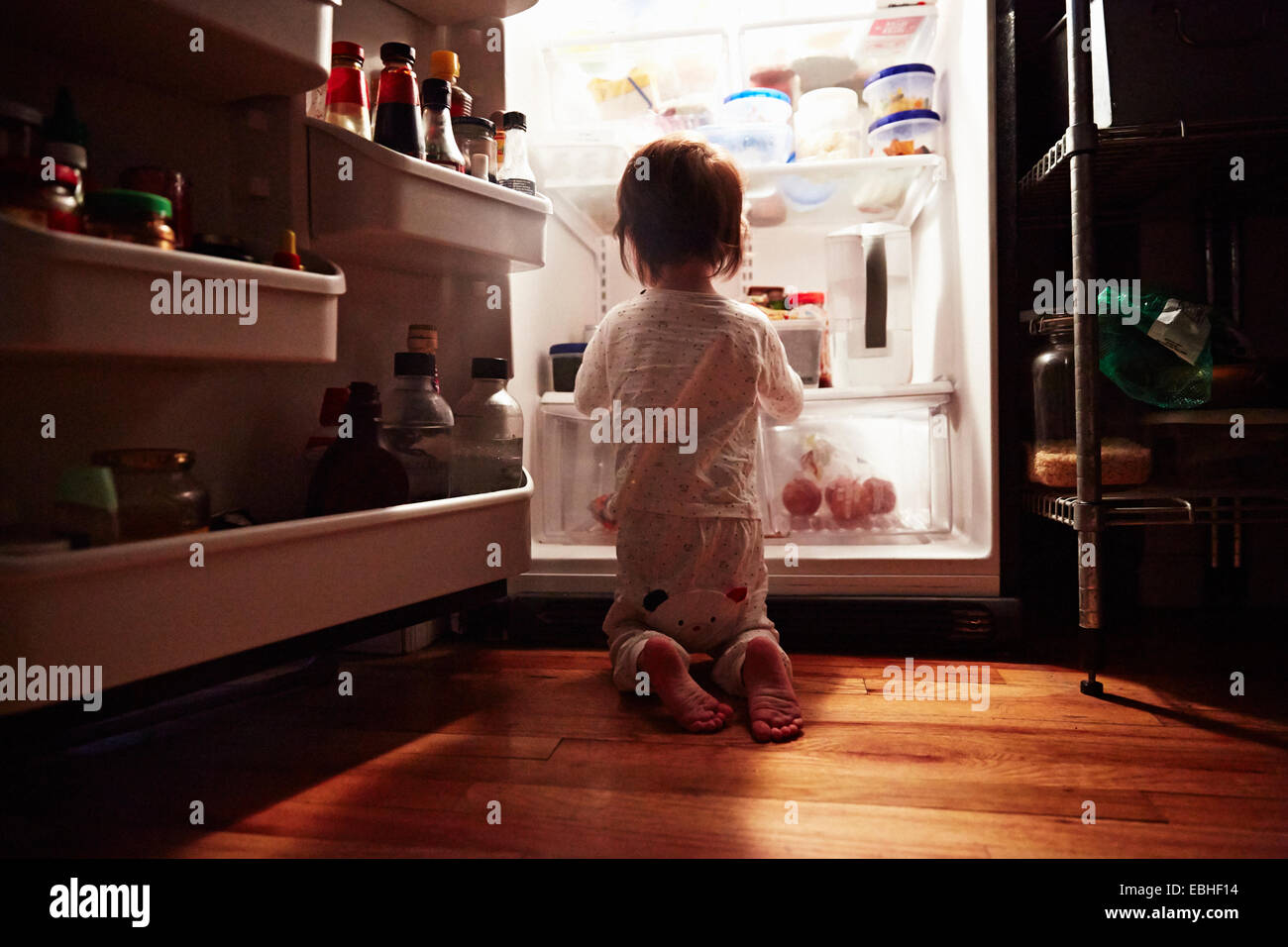 Rückansicht des männlichen Kleinkind kniend vor offenen Kühlschrank in der Nacht Stockfoto