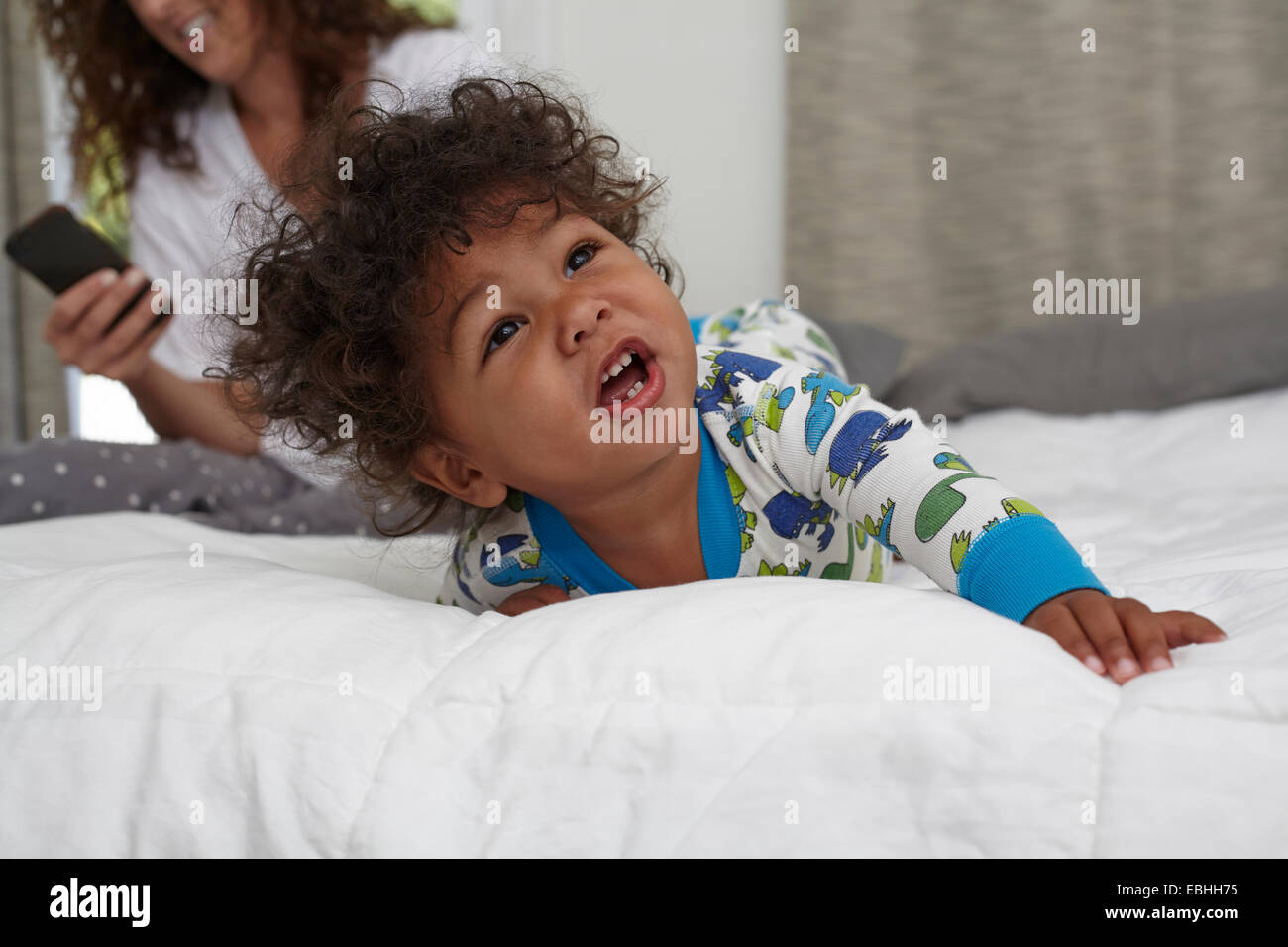 Männliche Kleinkind krabbeln auf Bett während Mutter mit smartphone Stockfoto
