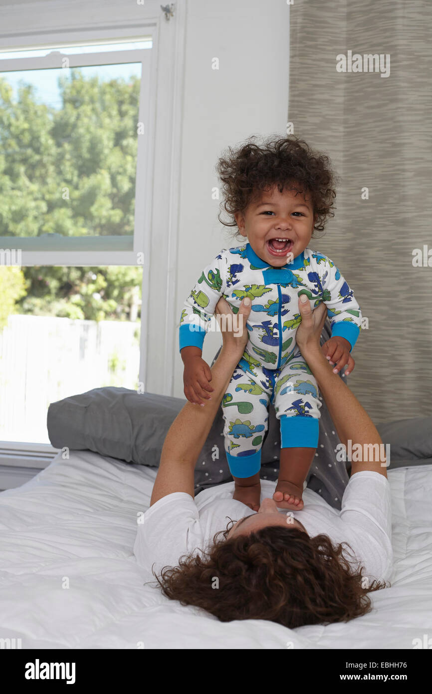 Junge Frau auf Bett Kleinkind Sohn hochhalten Stockfoto