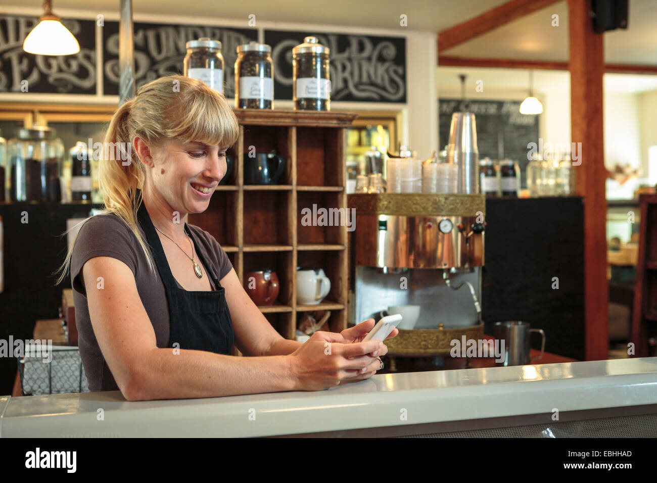 Weibliche Verkäuferin SMS auf Smartphone im Land laden-café Stockfoto