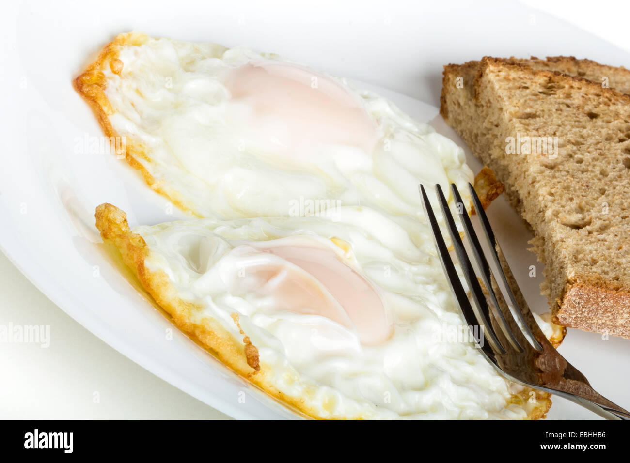 Zwei Eiern und Brot auf einem weißen Teller mit Gabel Stockfoto