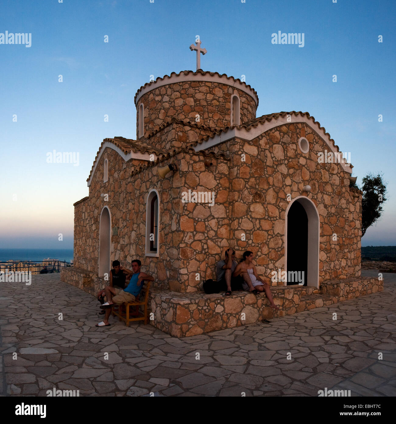 Touristen sitzen außerhalb der Kirche Prophet Eliah (Profitis Ilias) bei Sonnenuntergang. Stadt von Protaras, Zypern. Stockfoto