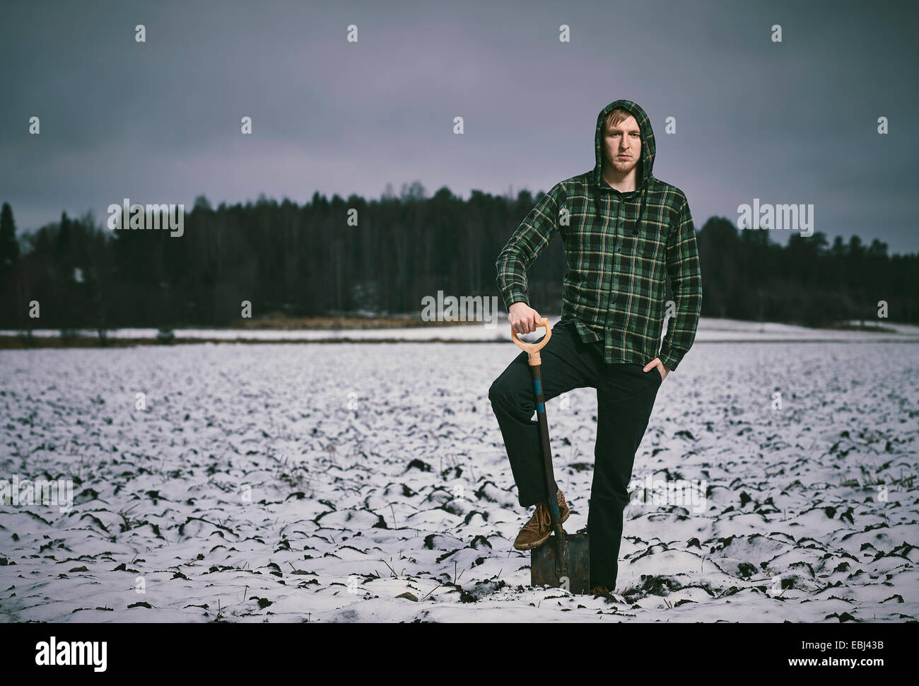 Hübscher junger Mann und Schaufel, verschneiten gepflügtes Feld auf Hintergrund - Kreuz bearbeitetes Bild Stockfoto