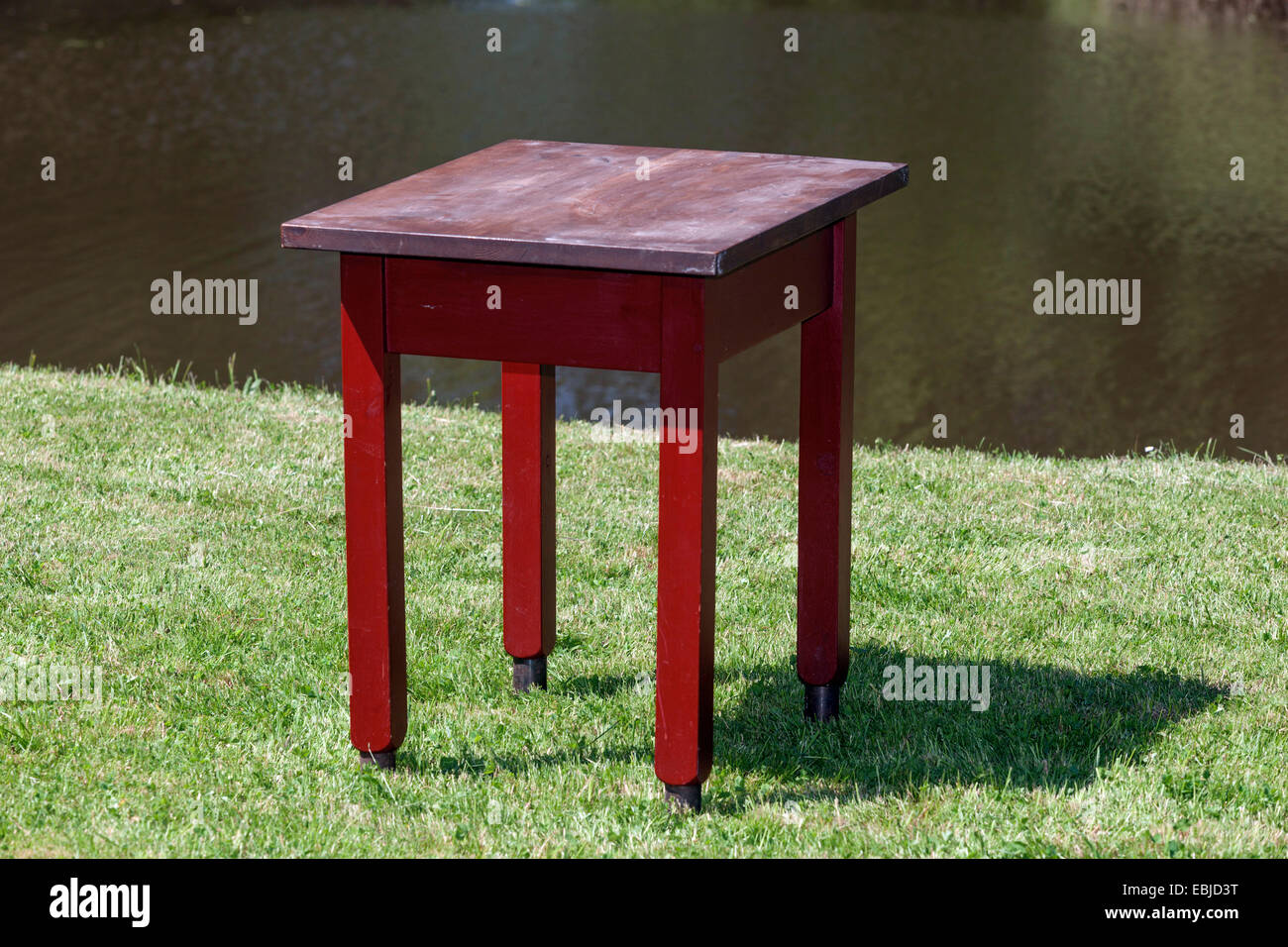 Roter Holztisch auf einer Wiese, Hintergrundwasser Stockfoto