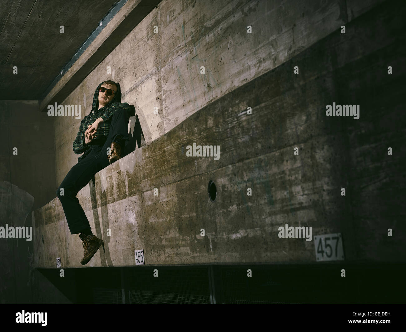 Junger Mann mit einer Sonnenbrille und er lehnt sich gegen eine Betonwand - Kreuz bearbeitete Bild, urban Design Stockfoto