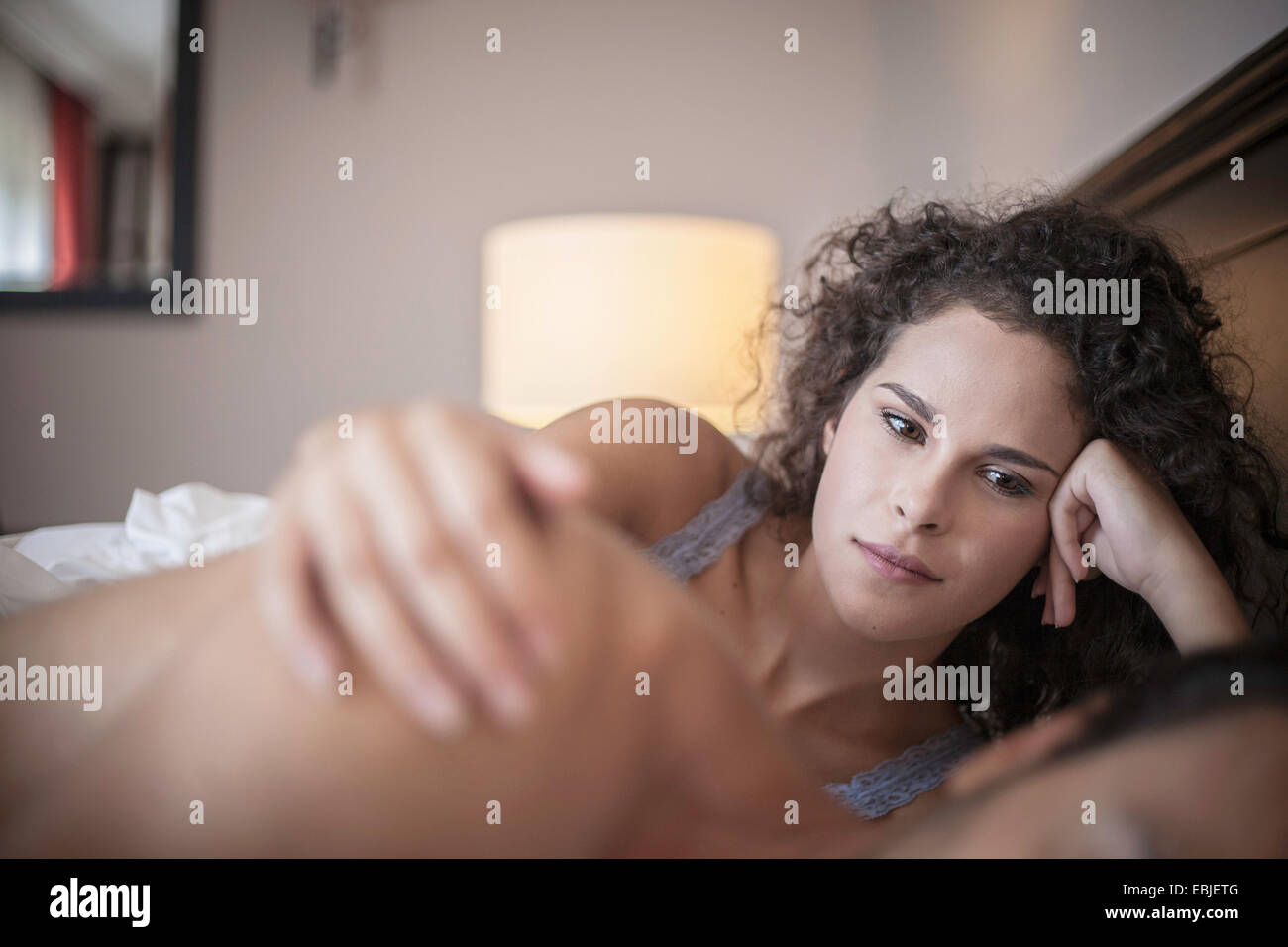 Junge Frau im Bett mit der Hand auf die Schulter des Mannes Stockfoto