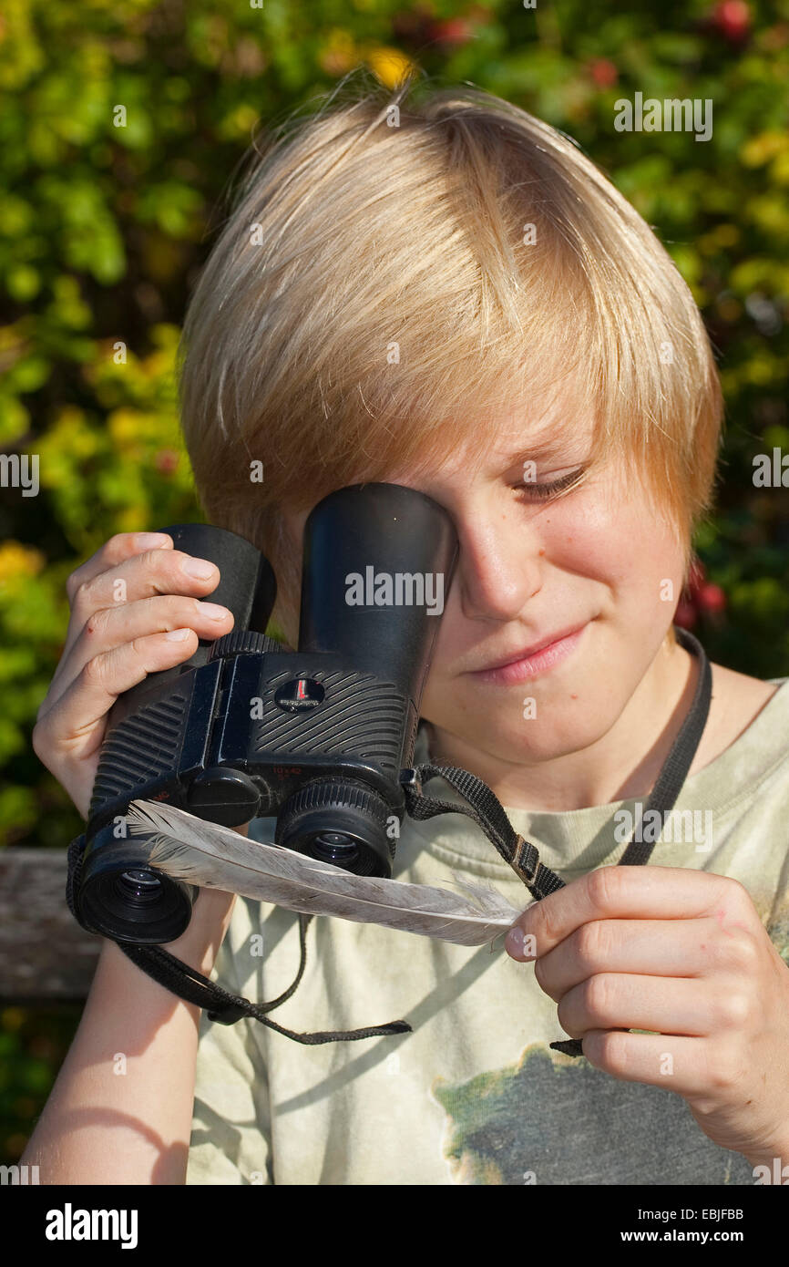 Junge mit einem umgekehrten Fernglases als eine Lupe und schaut auf eine Feder, Deutschland Stockfoto