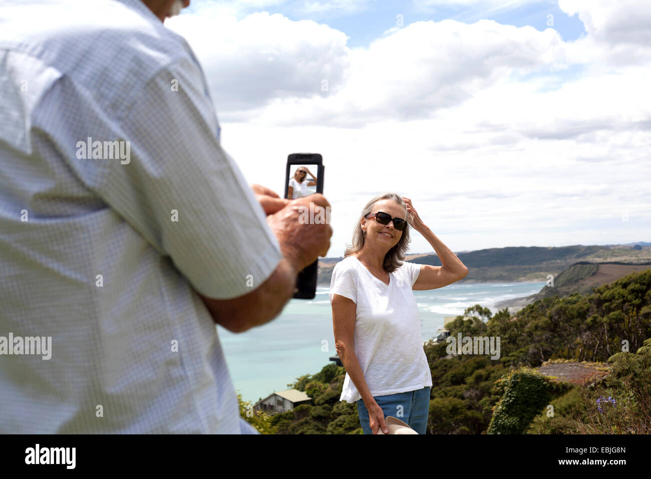 Mann fotografiert Frau, Ozean im Hintergrund, Raglan, Neuseeland Stockfoto