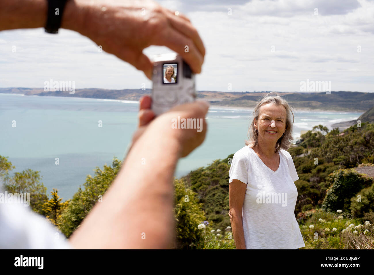 Mann fotografiert Frau, Ozean im Hintergrund, Raglan, Neuseeland Stockfoto