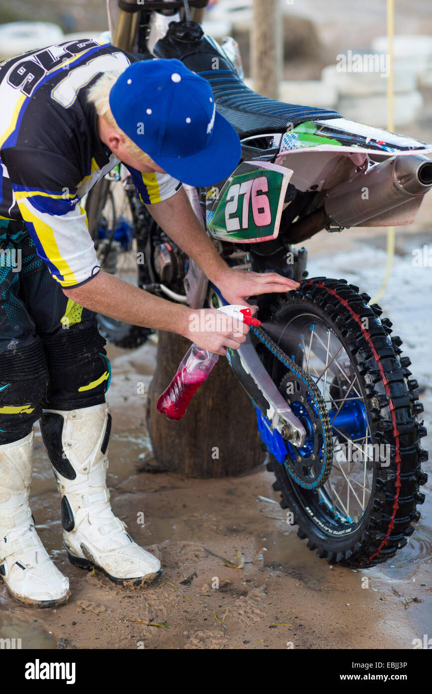 Junge männliche Motocross Wettbewerber nach vorne lehnen und Reinigung Motorrad Stockfoto