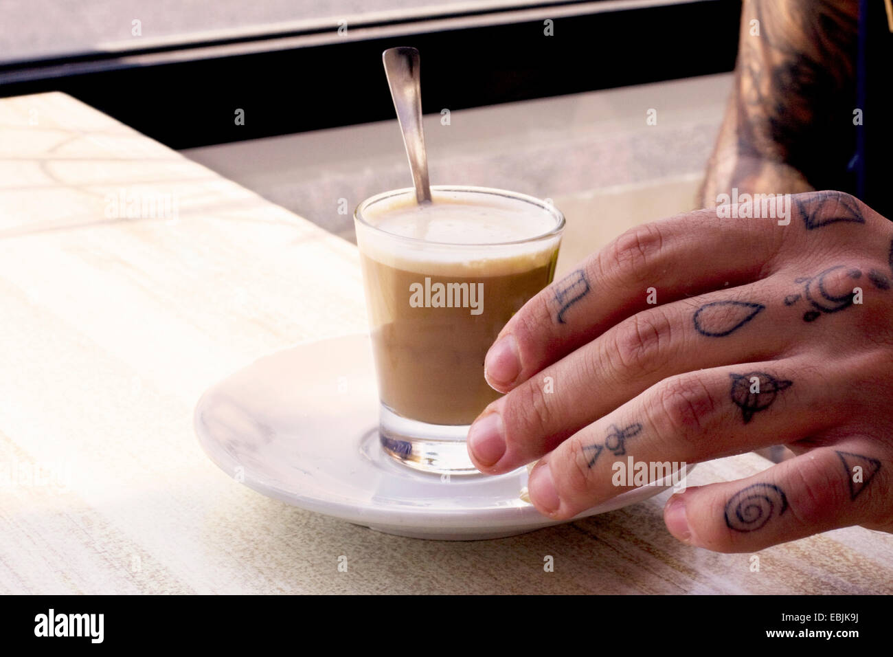 Tätowierte Hand des jungen Mannes und Kaffee Shotglas am Café-Tisch Stockfoto