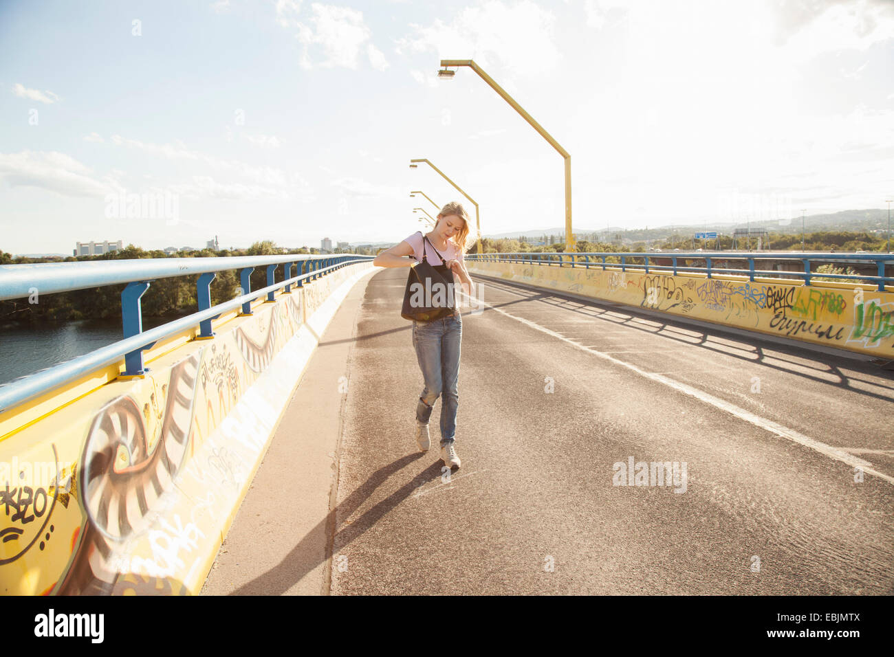 Junge Frau, die zu Fuß über die Brücke suchen in Umhängetasche Stockfoto